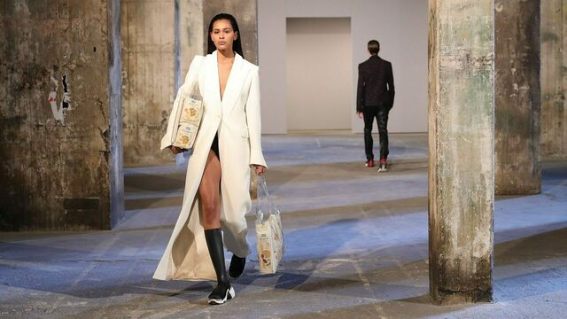 Ein Model in weißem Mantel läuft mit transparenten Taschen gefüllt mit Pasta über den Catwalk.