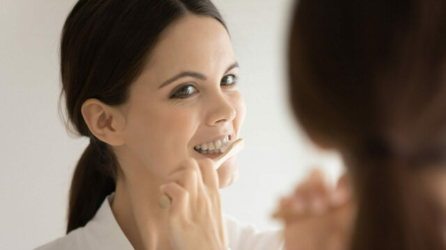 Eine Frau putzt sich die Zähne und schaut dabei in den Spiegel.