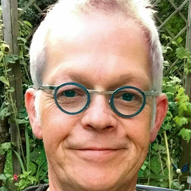 Das Gesicht eines Mannes mit grauen Haaren und runder Brille.