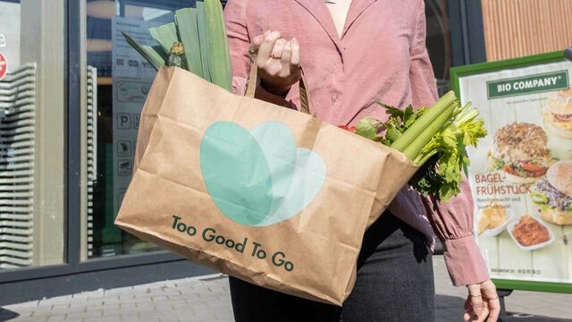 Eine Frau hält eine Papiertüte mit der Aufschrift "Too Good To Go" in der Hand.