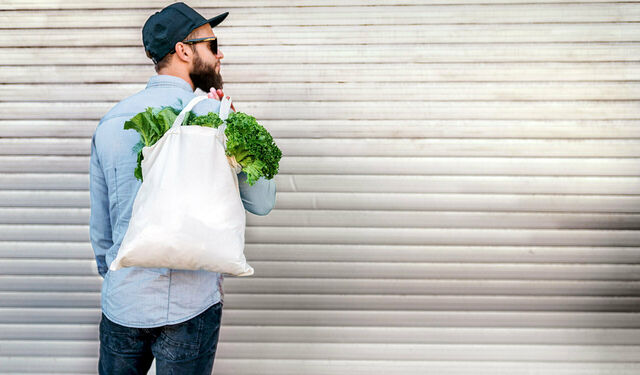 Mann mit Sonnenbrille und Kappe trägt eine Jutetasche mit Gemüse über seiner Schulter.