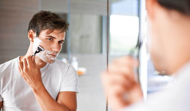 Ein Mann steht vor dem Spiegel und rasiert seinen Bart.
