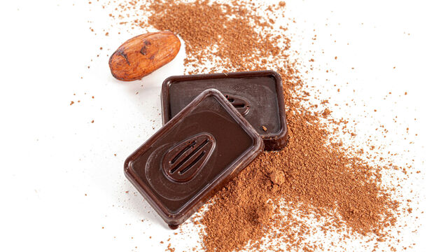 Zwei Stückchen dunkler Schokolade auf etwas verstreutem Kakaopulver angerichtet